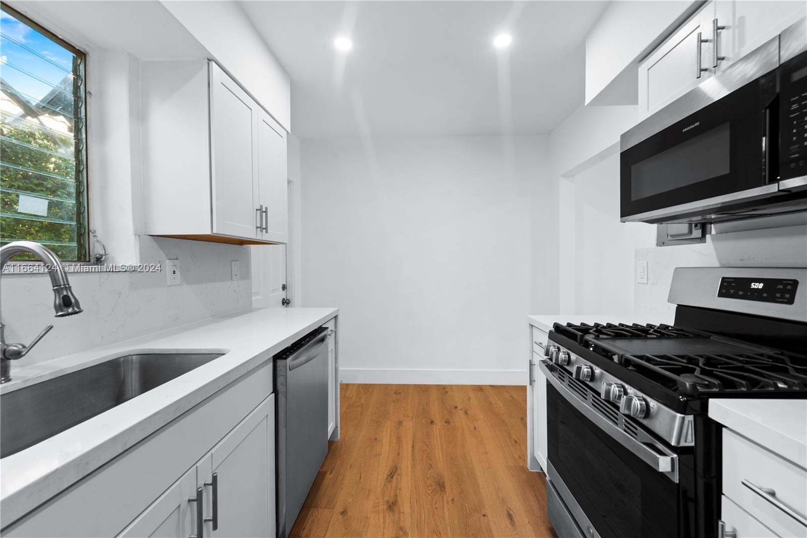 a kitchen with stainless steel appliances a sink dishwasher stove and microwave with wooden floor