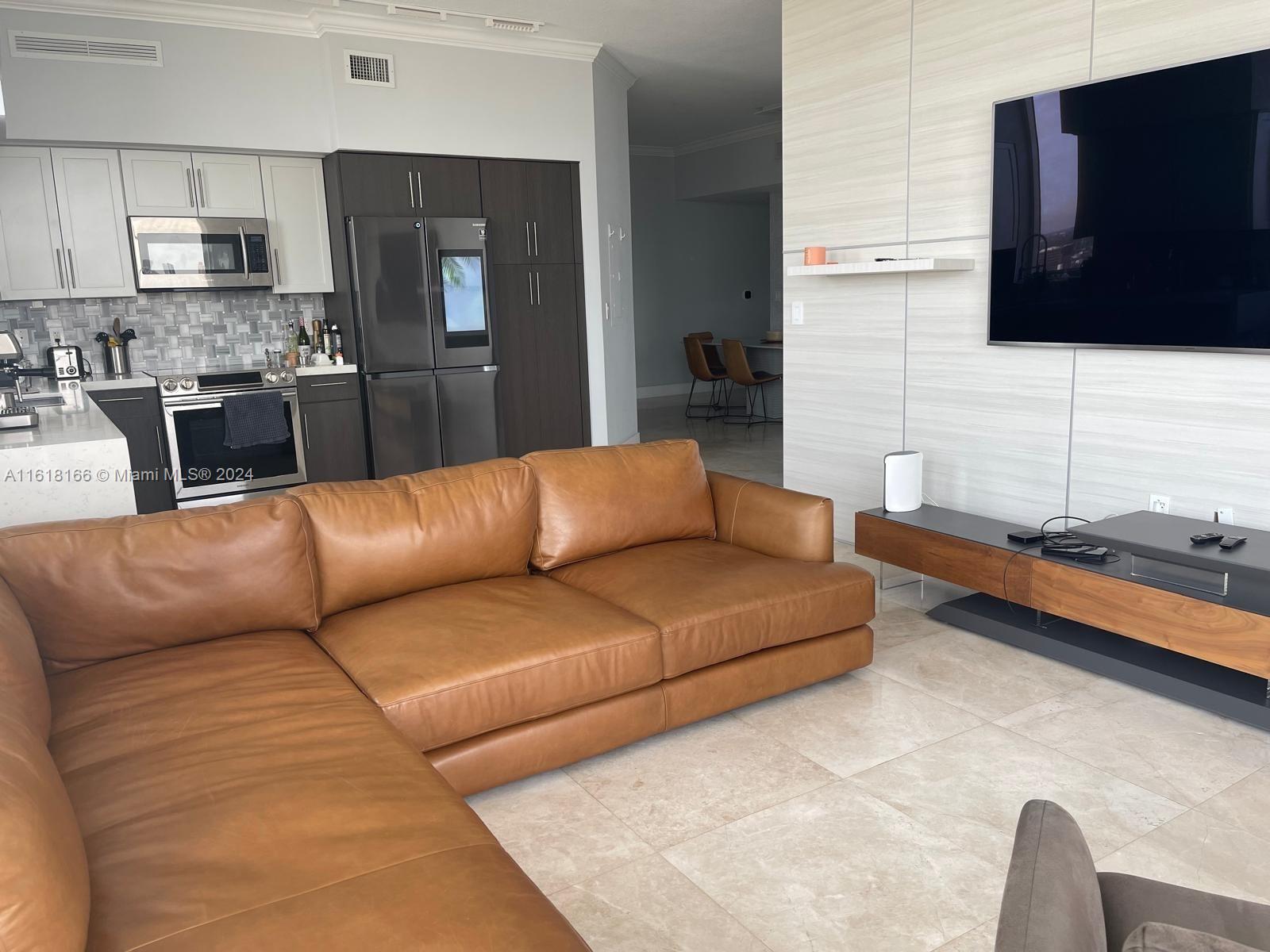 a living room with stainless steel appliances kitchen island granite countertop a couch and a flat screen tv