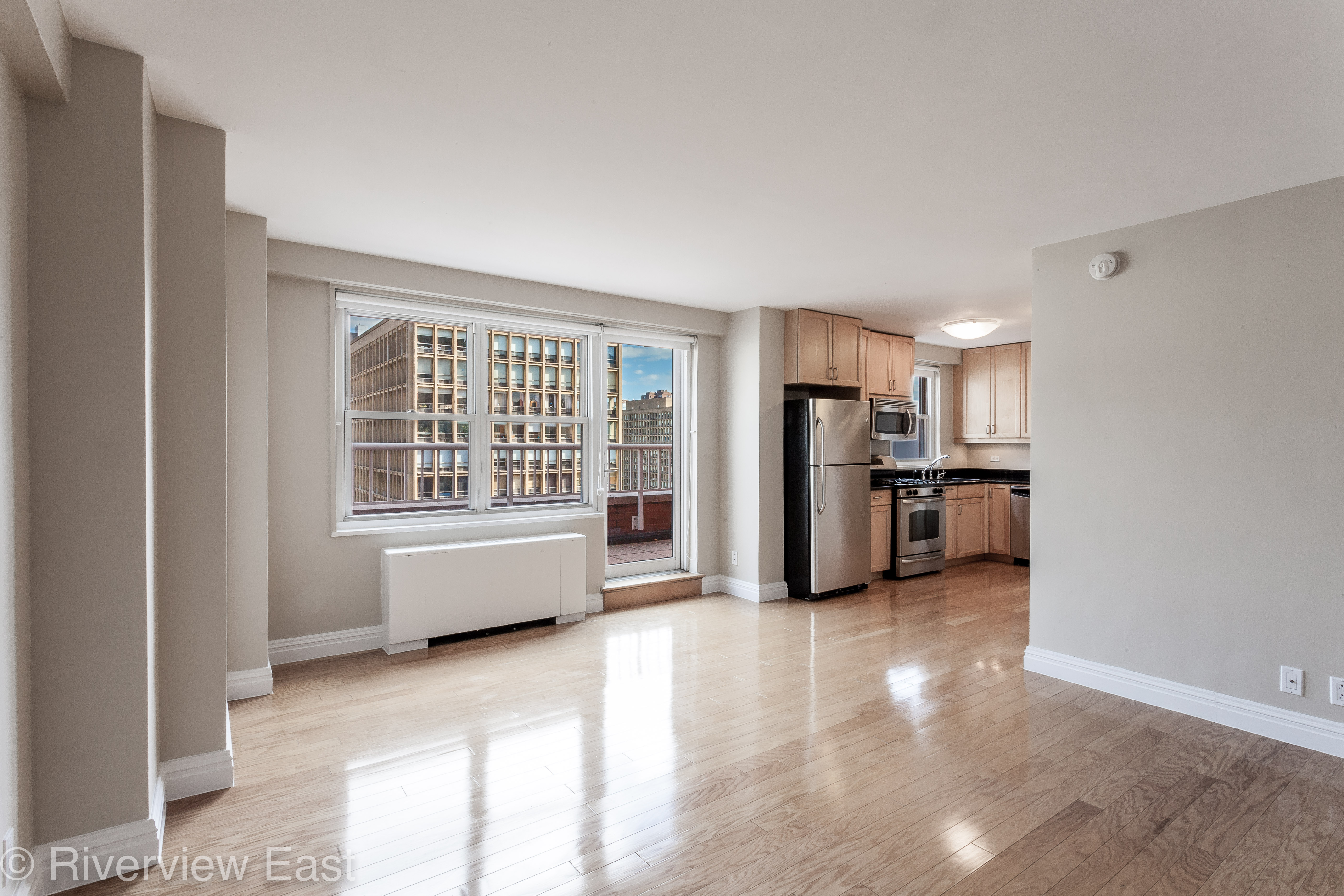 a living room with stainless steel appliances kitchen island granite countertop a stove a refrigerator a sink a microwave with wooden floor and cabinets