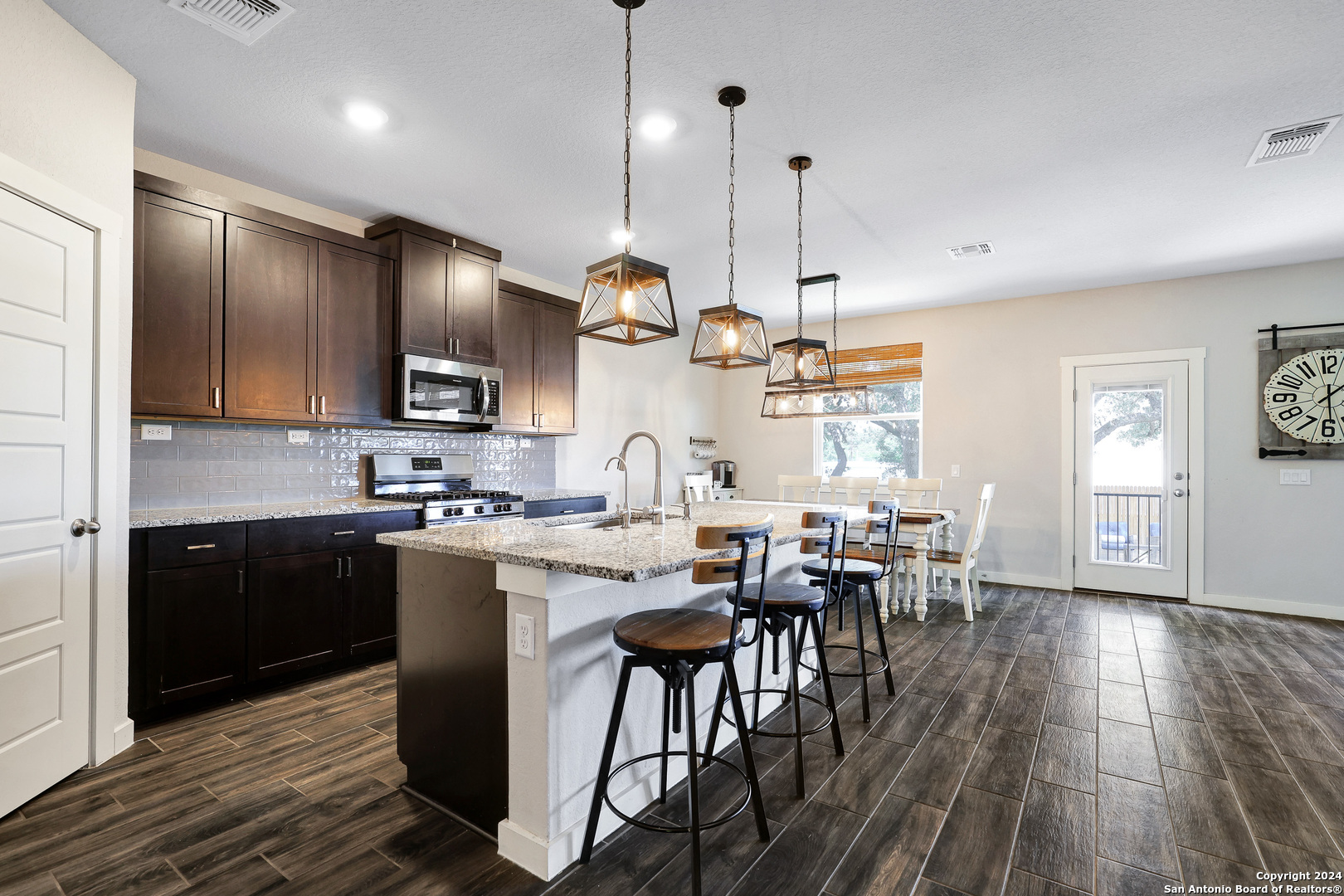 a open kitchen with stainless steel appliances granite countertop a stove top oven a sink dishwasher a dining table and chairs with wooden floor