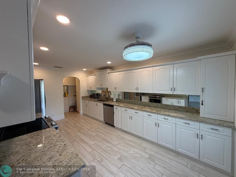 a open kitchen with stainless steel appliances granite countertop a sink dishwasher stove and white cabinets with wooden floor