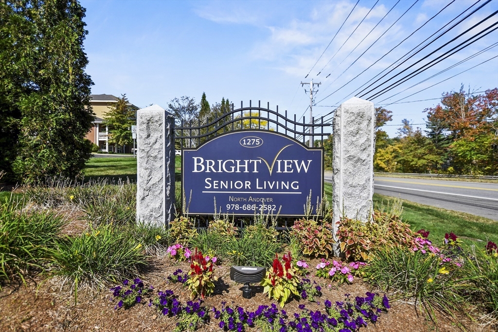 a sign board with flower plants and wooden fence