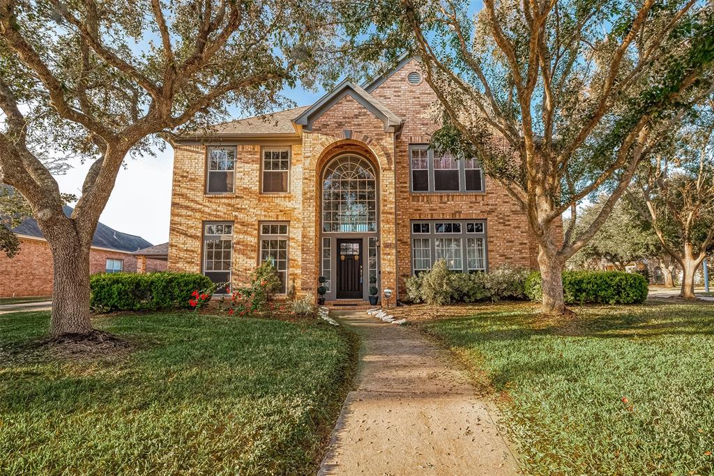 This charming two-story brick home features a welcoming arched entryway, large windows, and a well-maintained front yard with mature trees, offering plenty of curb appeal.