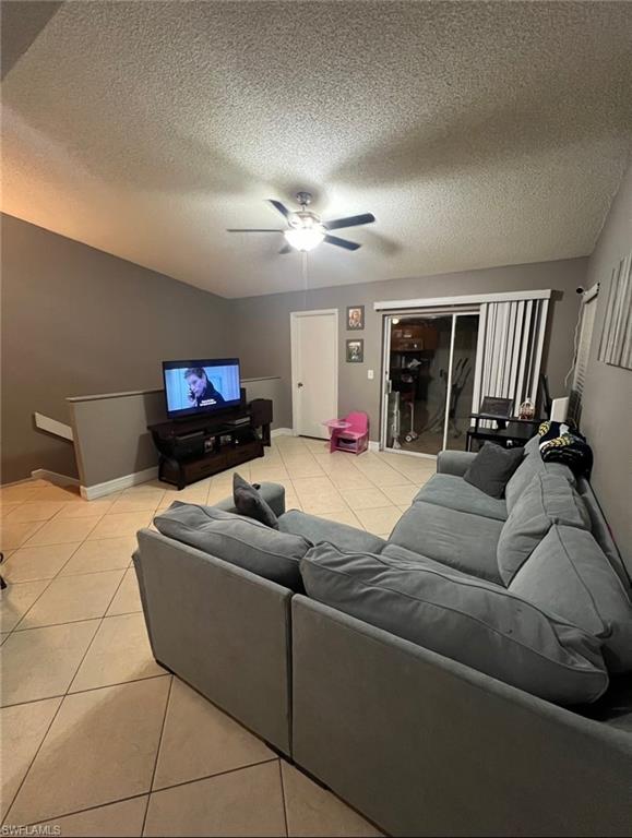 Living room with ceiling fan, light tile patterned flooring, and a textured ceiling