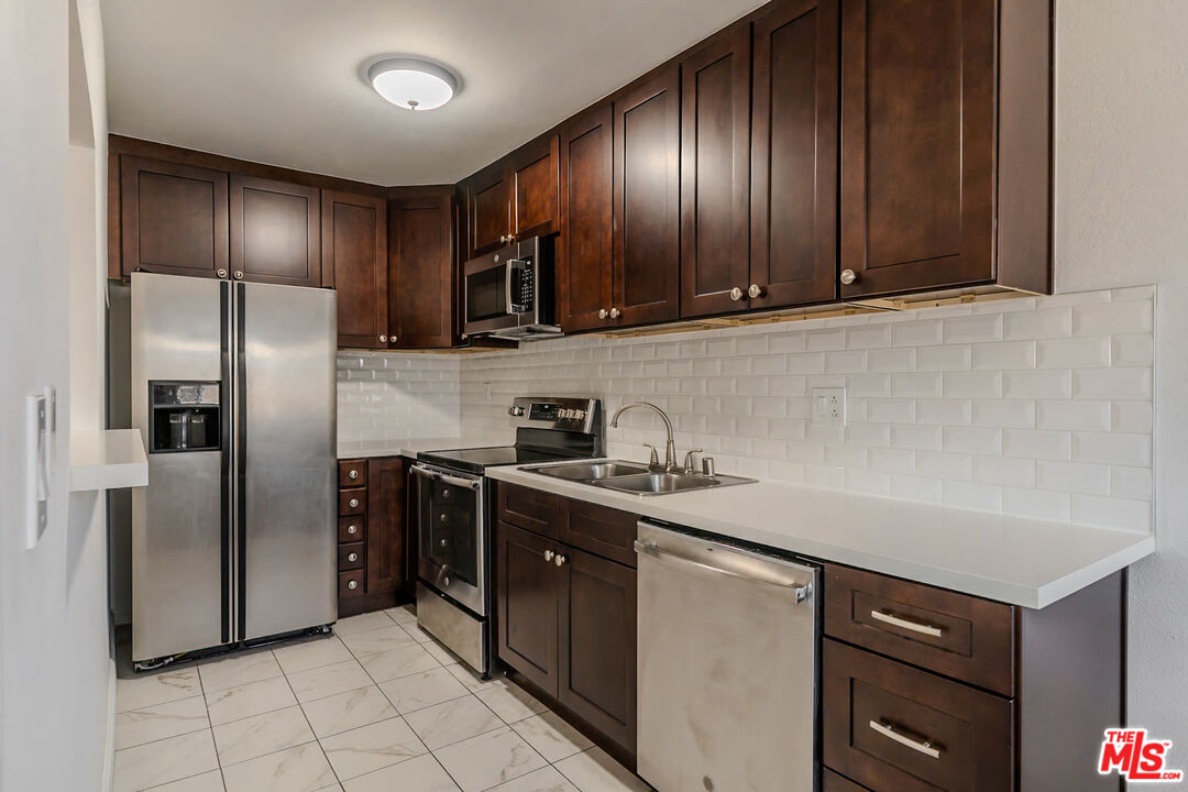 a kitchen with stainless steel appliances granite countertop wood cabinets a sink and a refrigerator