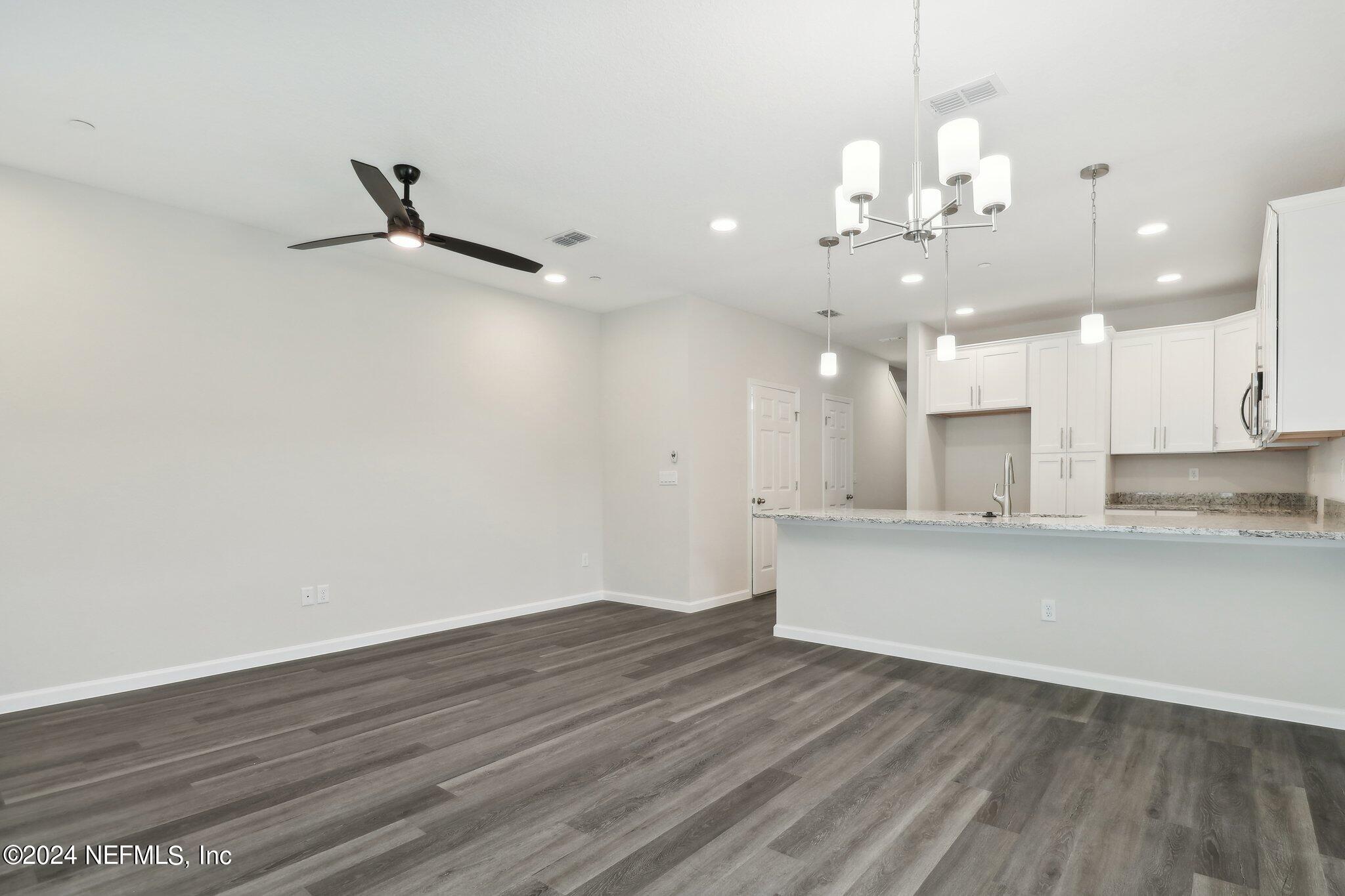 an empty room with wooden floor and kitchen view