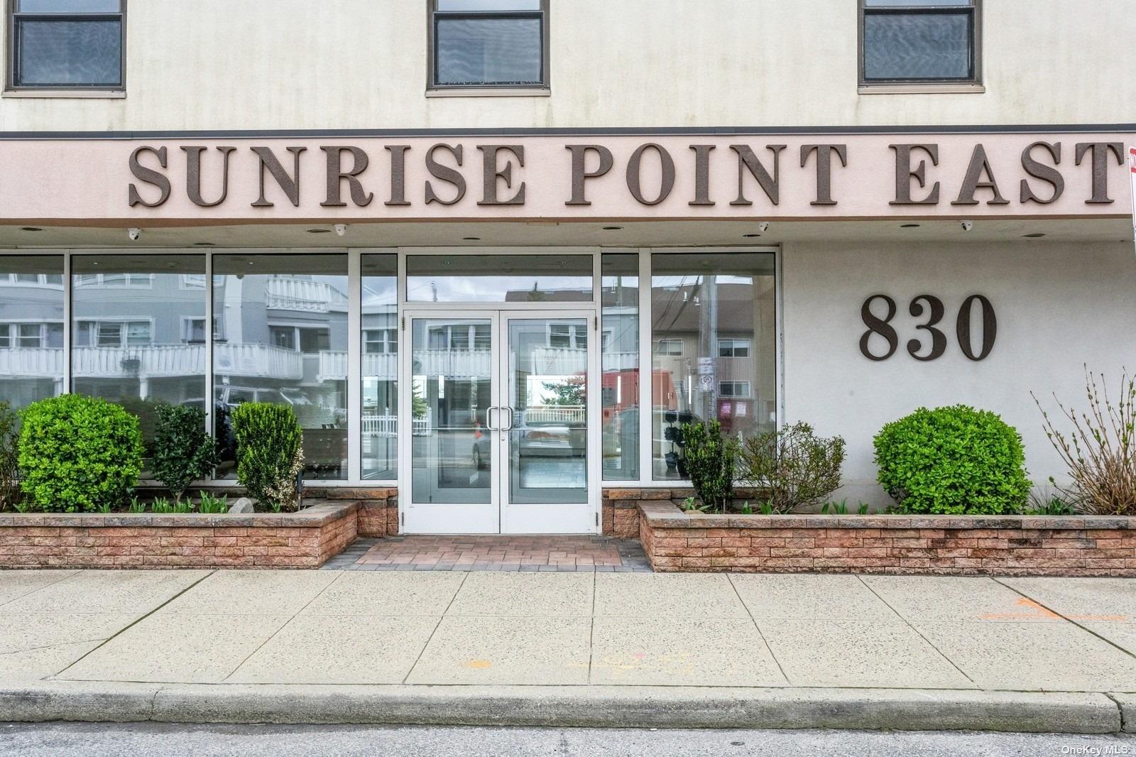 a front view of a building with retail windows and plants