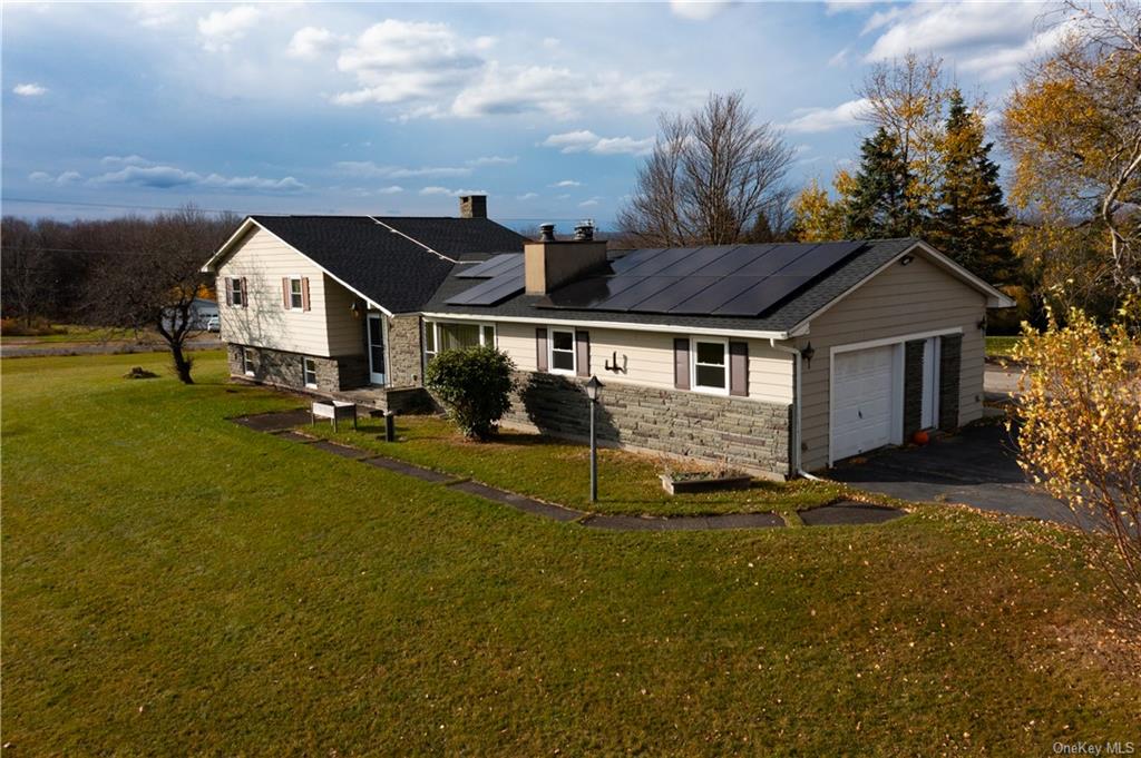 View of front of home with a front yard, a garage, and solar panels