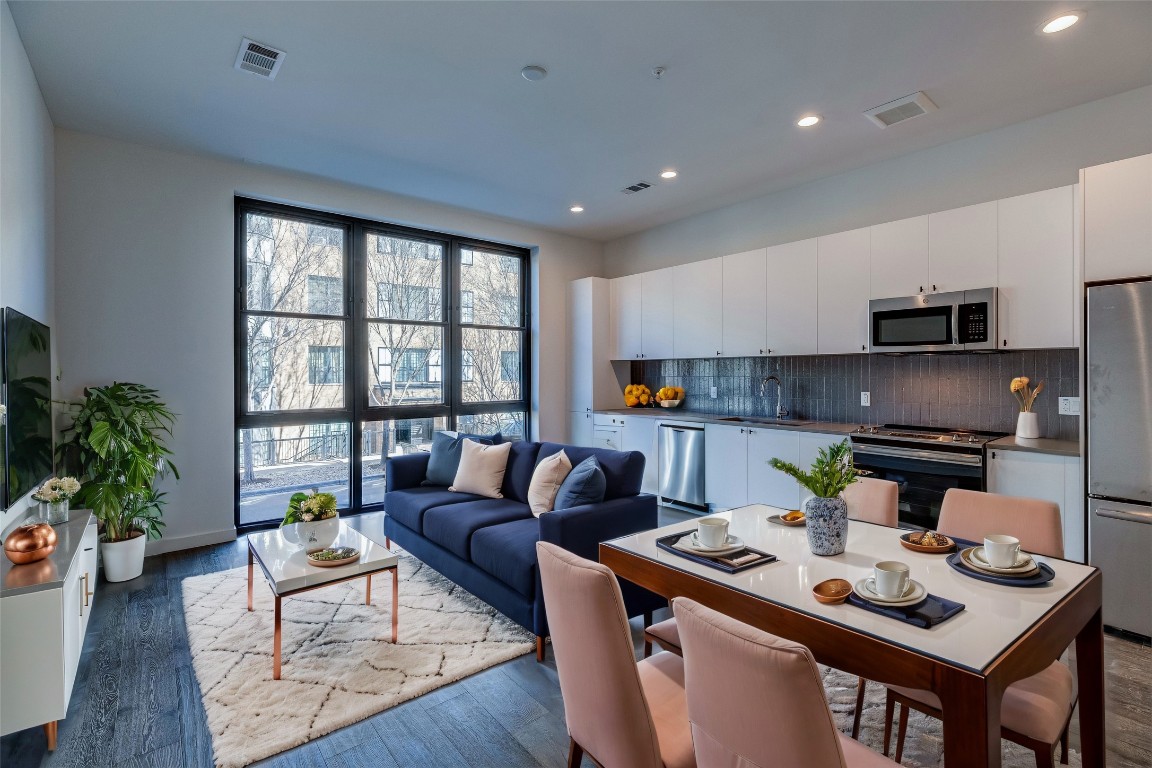 a living room with stainless steel appliances furniture a rug and a kitchen view