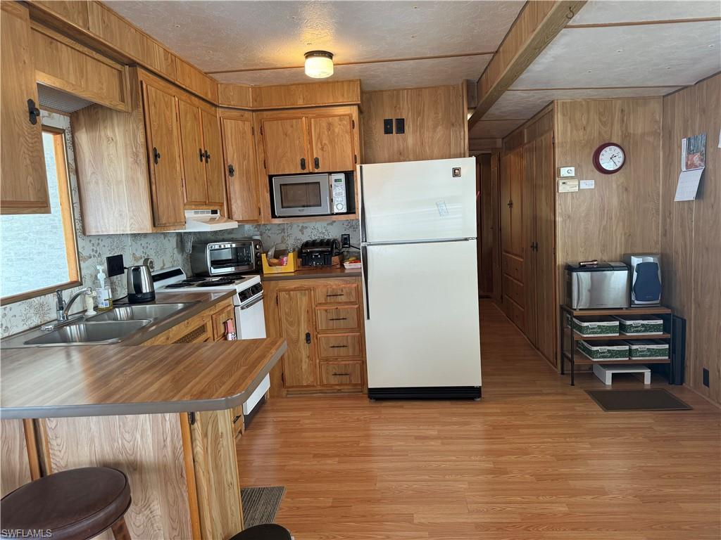 Kitchen featuring sink, stainless steel appliances, a kitchen bar, wooden walls, and light wood-type flooring