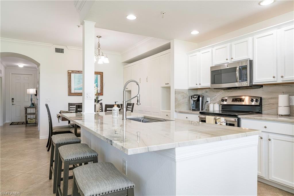 Kitchen featuring a center island with sink, pendant lighting, a notable chandelier, appliances with stainless steel finishes, and white cabinets.