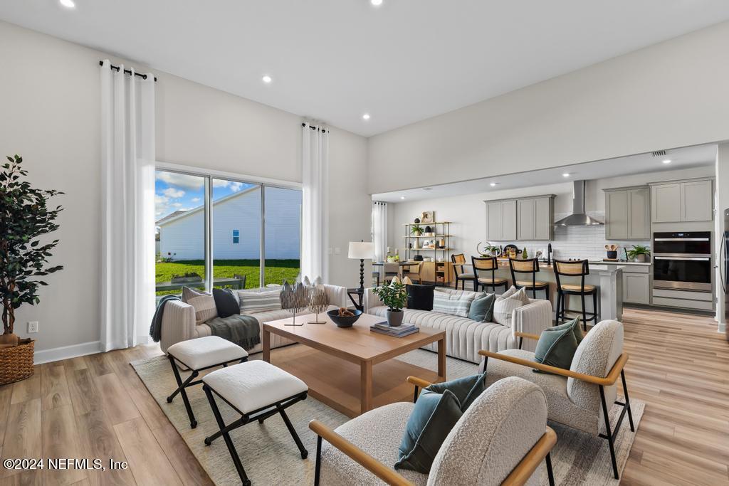 a living room with lots of furniture kitchen view and a large window