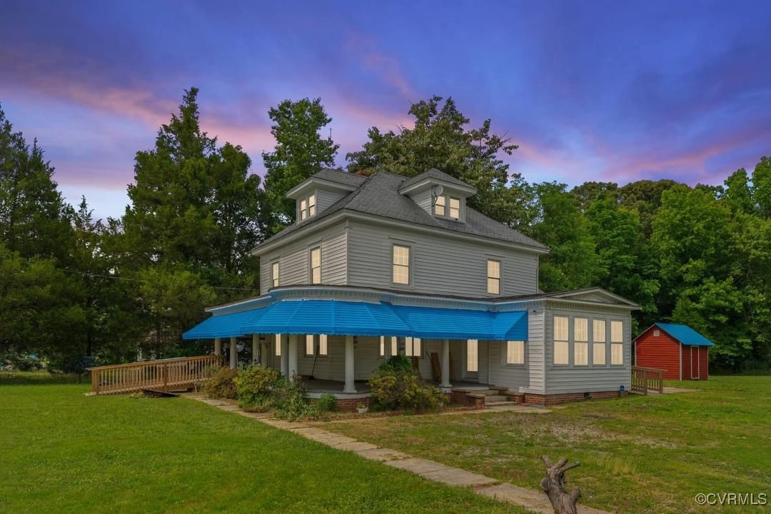 Back house at dusk with covered porch, a lawn, and