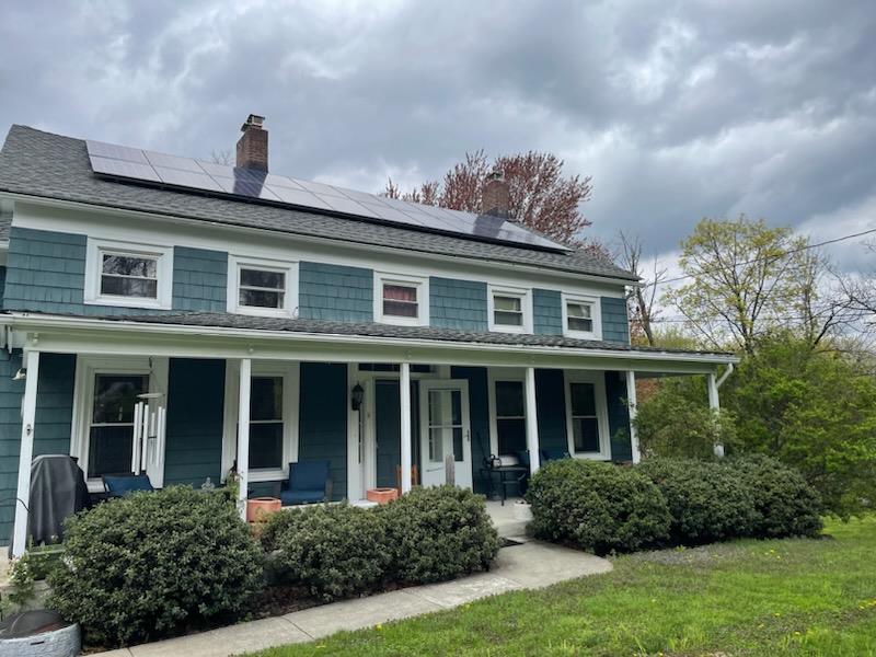 View of front facade with a front lawn, solar panels, and a porch