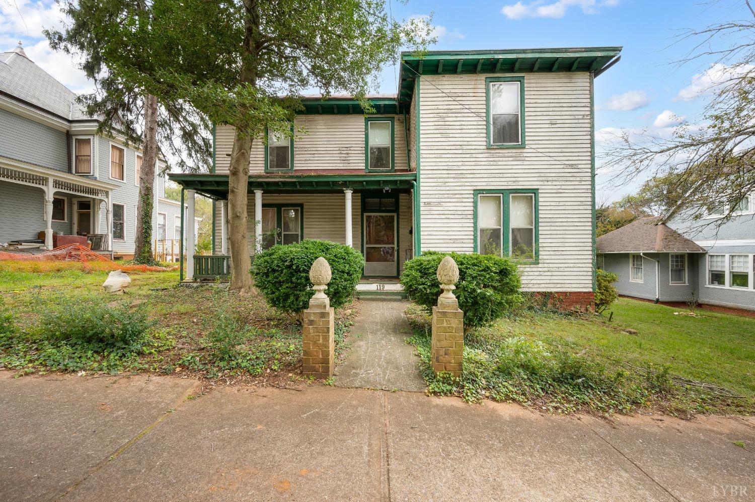 a view of a house with brick walls and a yard with plants and large trees