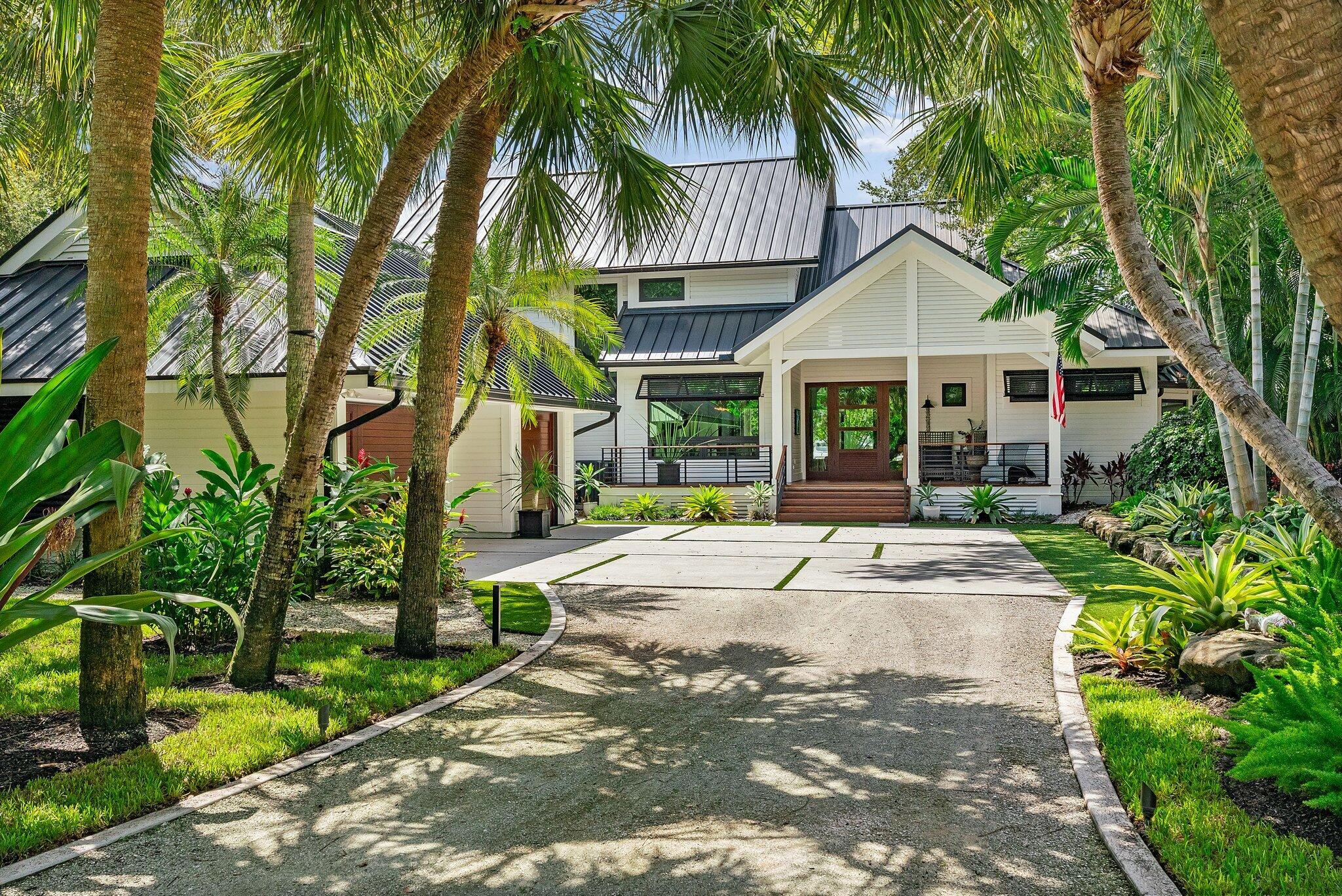 a view of a white house with a big yard plants and palm trees