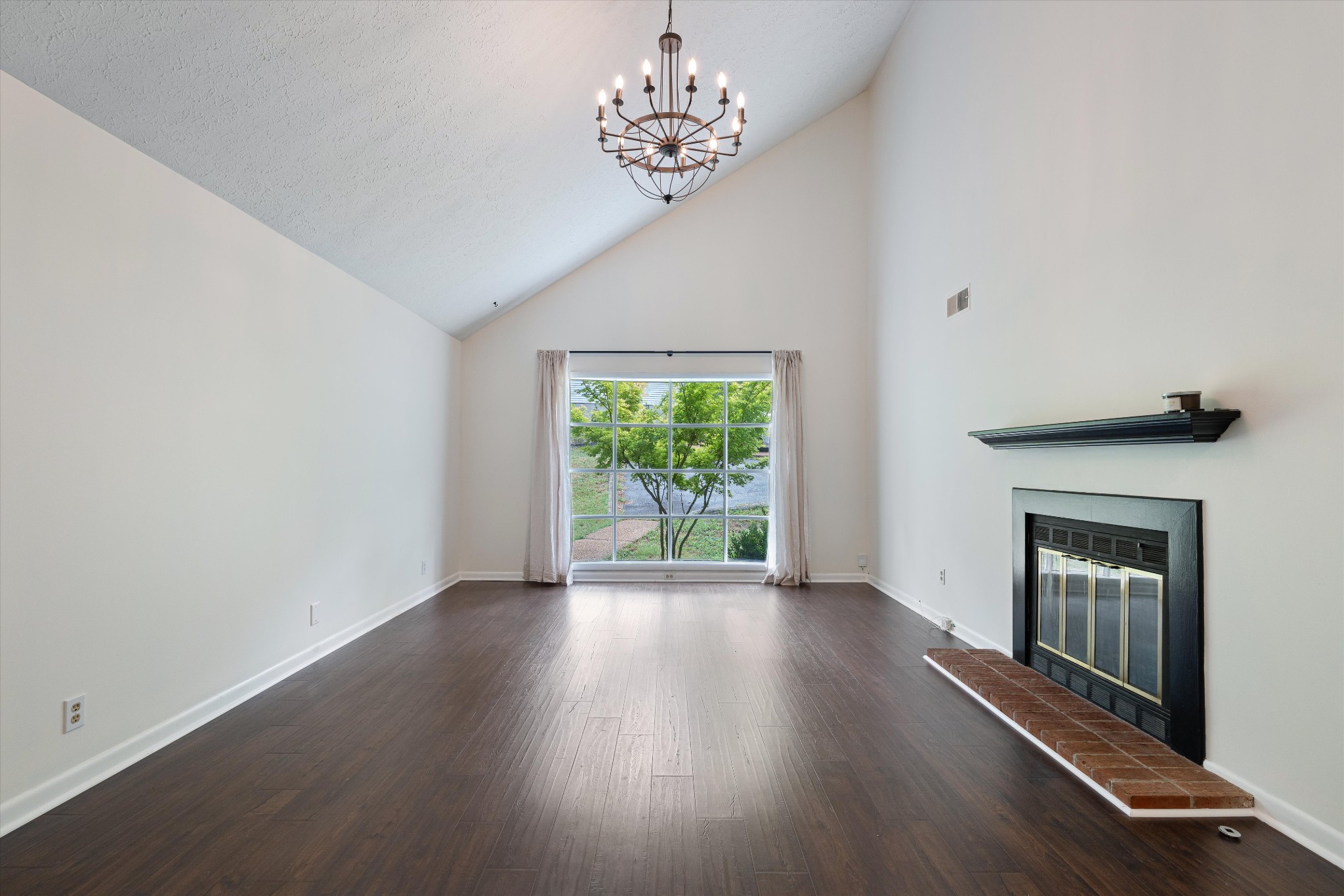 a view of an empty room with wooden floor fireplace and a window