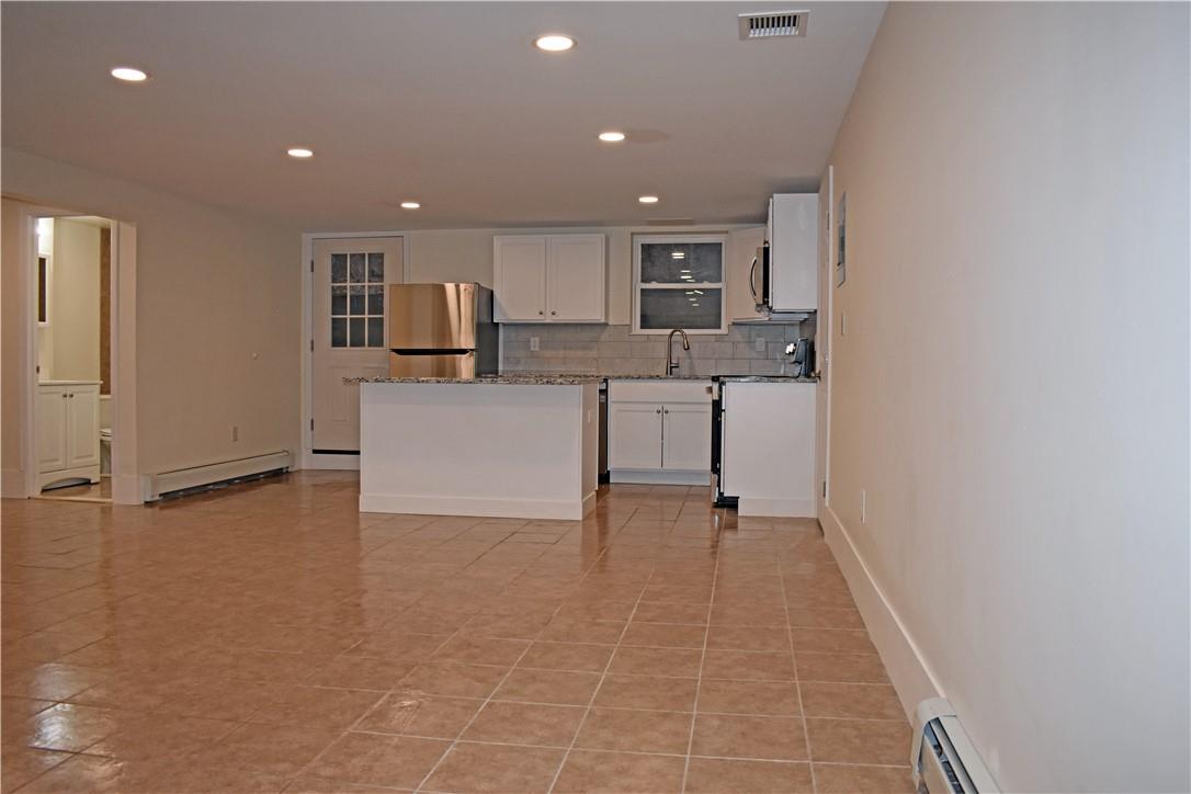 Kitchen with stainless steel fridge, white cabinets, tasteful backsplash, a baseboard radiator, and granite countertops