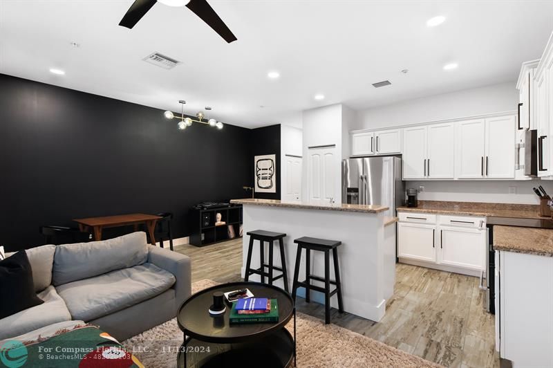 a kitchen with stainless steel appliances kitchen island granite countertop a refrigerator a stove a microwave oven a dining table and chairs with wooden floor