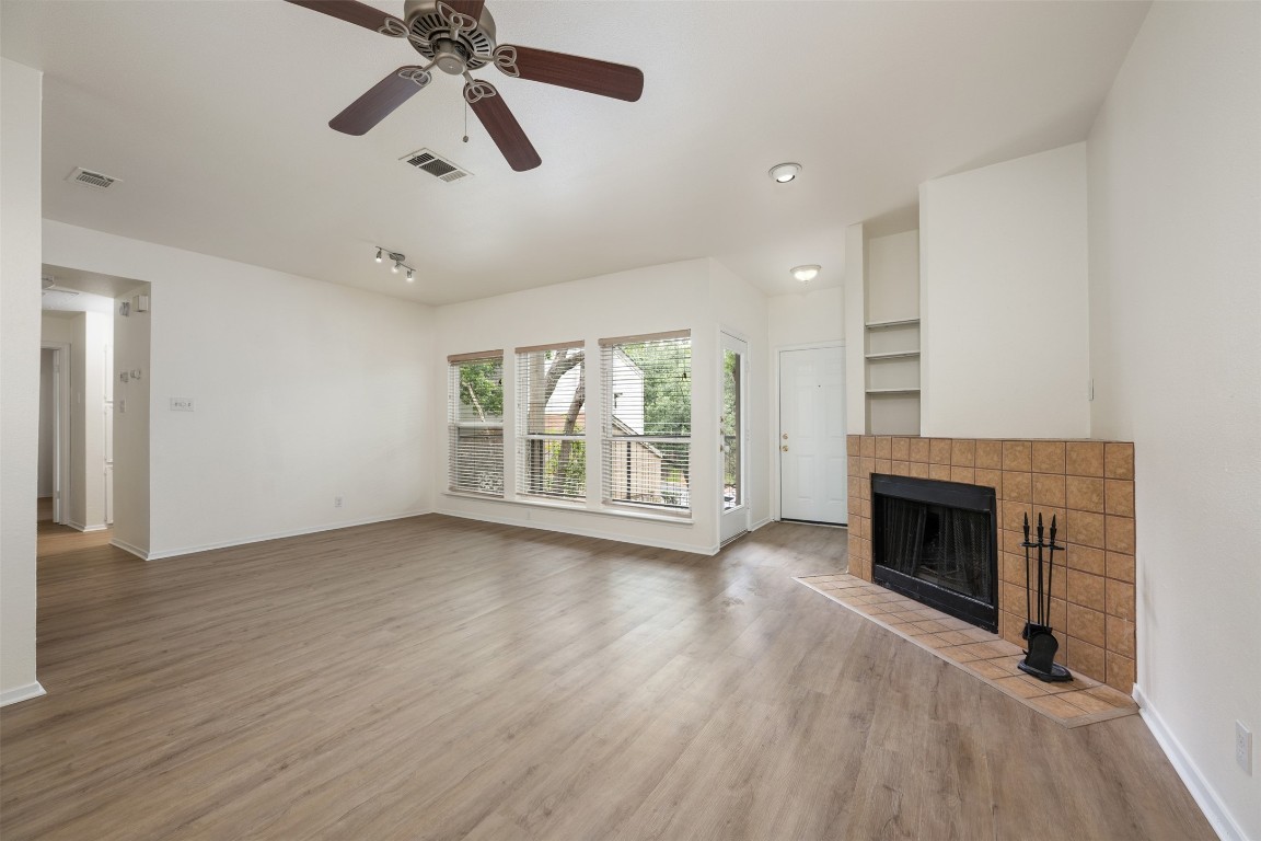 a view of an empty room with wooden floor fireplace and a window