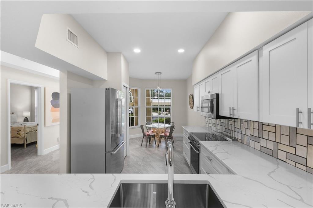 Kitchen with hanging light fixtures, white cabinetry, light stone countertops, and stainless steel appliances