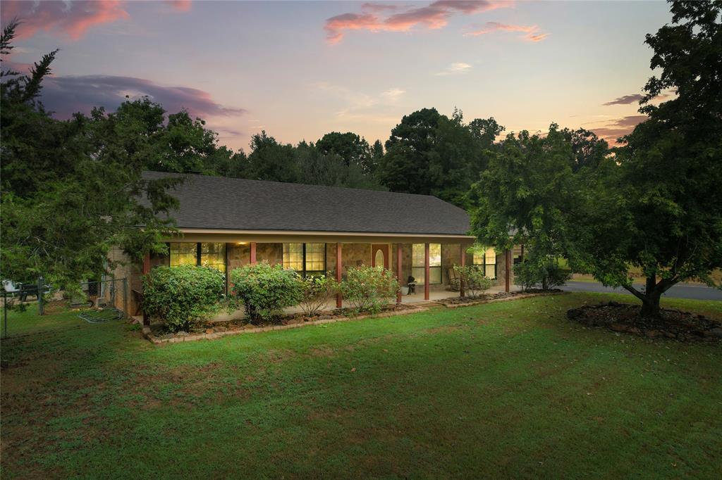 a view of house in front of a big yard with large trees