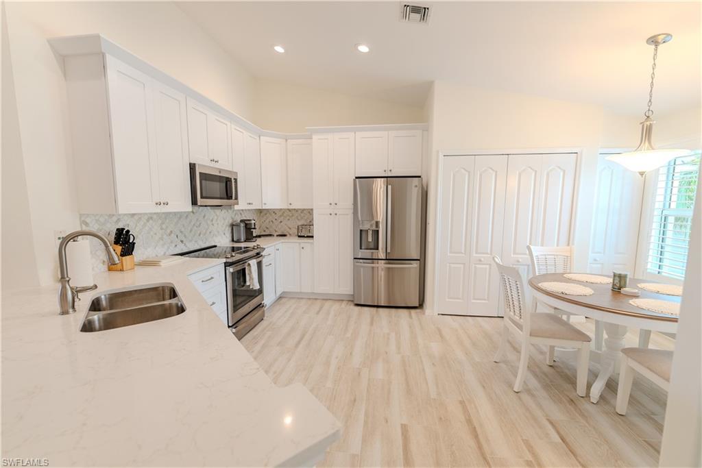 Kitchen with stainless steel appliances, white cabinets, sink, light stone countertops, and vaulted ceiling