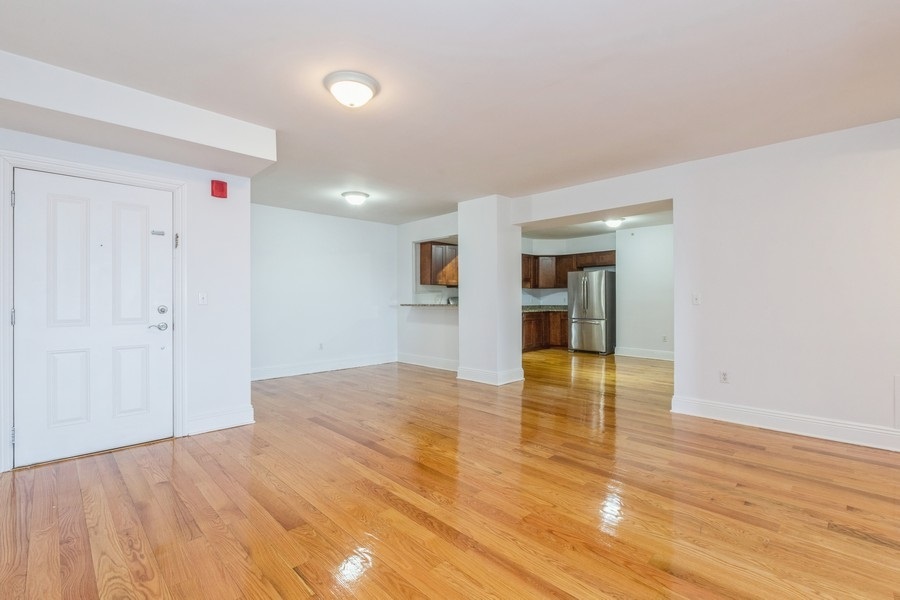 a view of empty room with wooden floor and kitchen