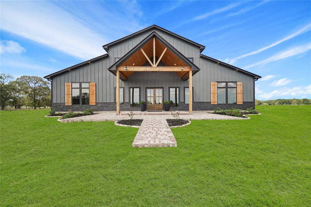 Modern farmhouse situated on 15 sprawling acres, featuring a sleek exterior, wooden accents, and a welcoming brick covered porch. Perfect for those seeking a blend of rustic charm and contemporary style.