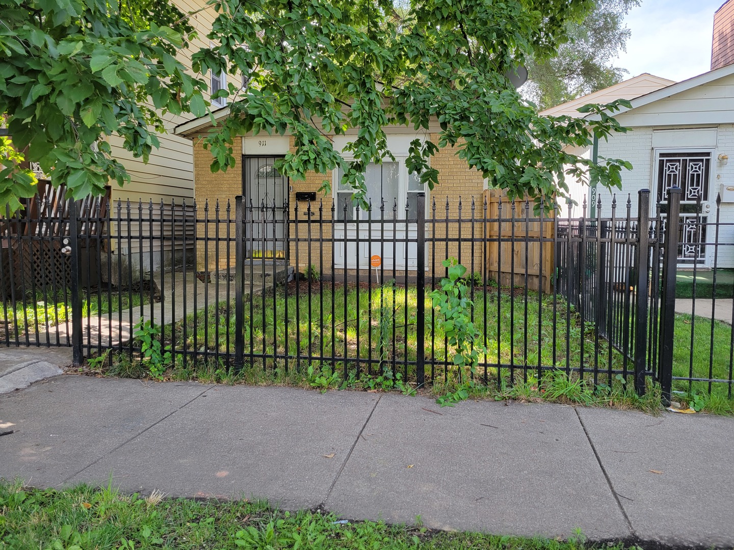 a view of a brick house in front of a yard with plants and large trees