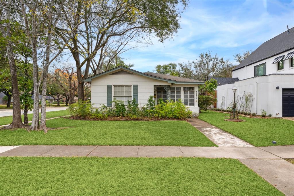 a view of a yard in front of a house with plants and large trees