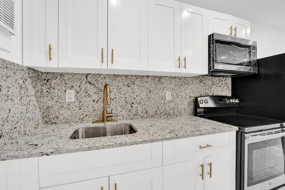 a kitchen with granite countertop white cabinets sink and stainless steel appliances