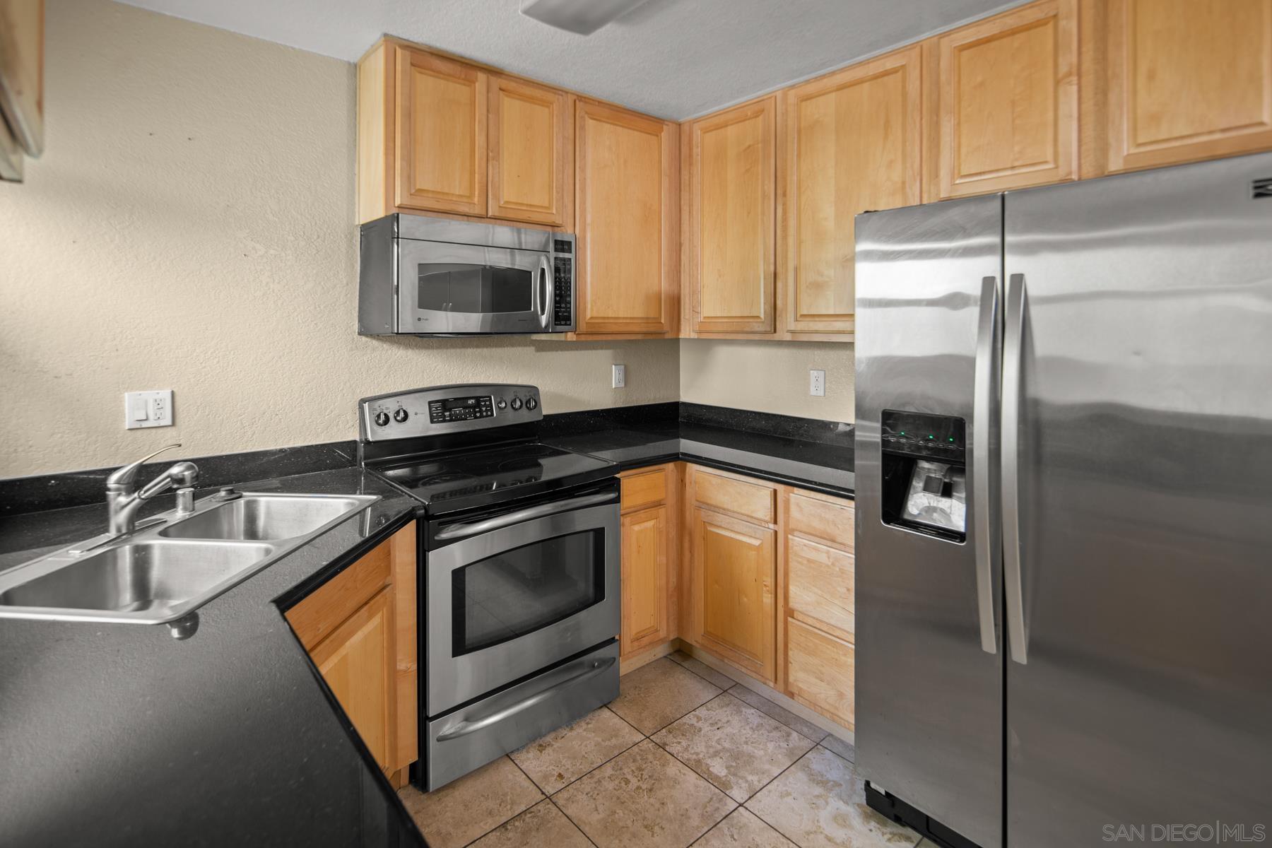 a kitchen with stainless steel appliances granite countertop a refrigerator a stove and a sink with wooden cabinet