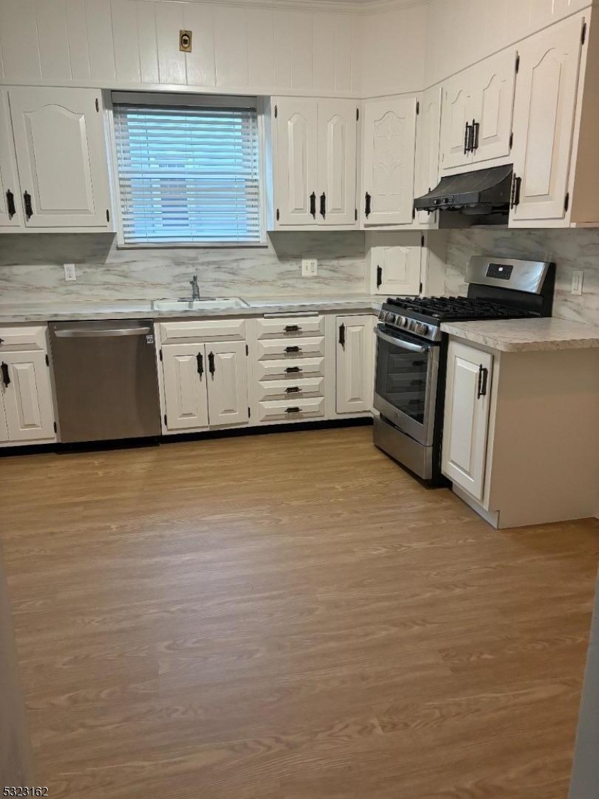 a kitchen with stainless steel appliances granite countertop a stove a sink and white cabinets