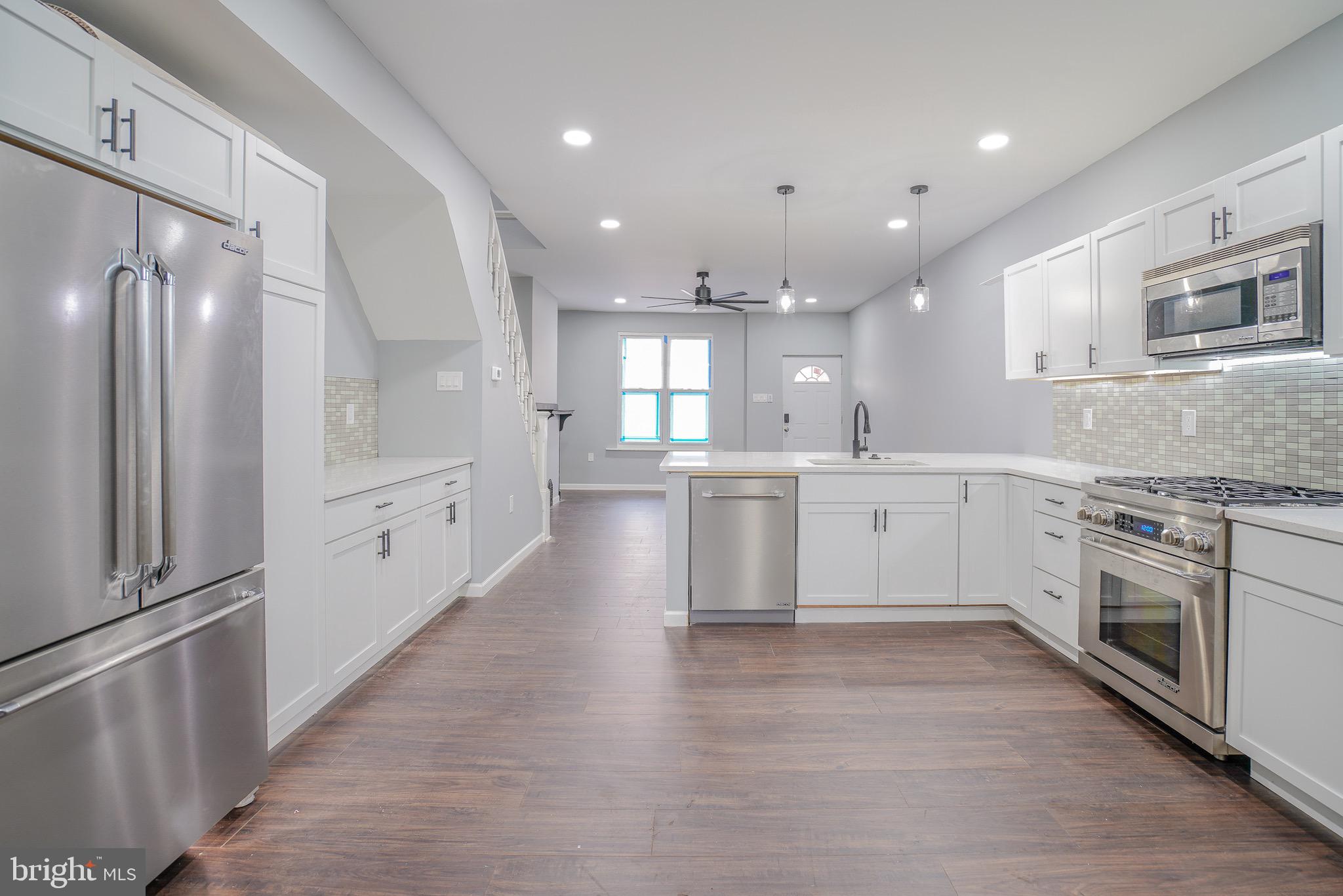 a large white kitchen with a large counter top space a sink stainless steel appliances and cabinets