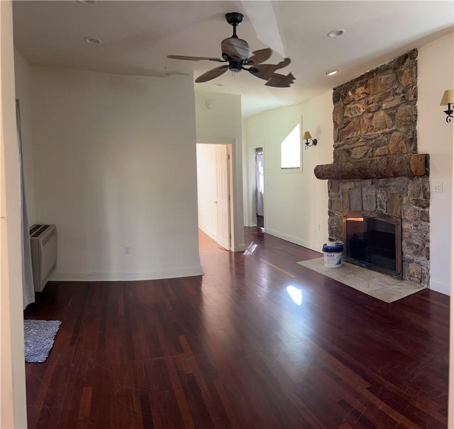 Unfurnished living room with hardwood / wood-style flooring, an AC wall unit, a fireplace, and ceiling fan