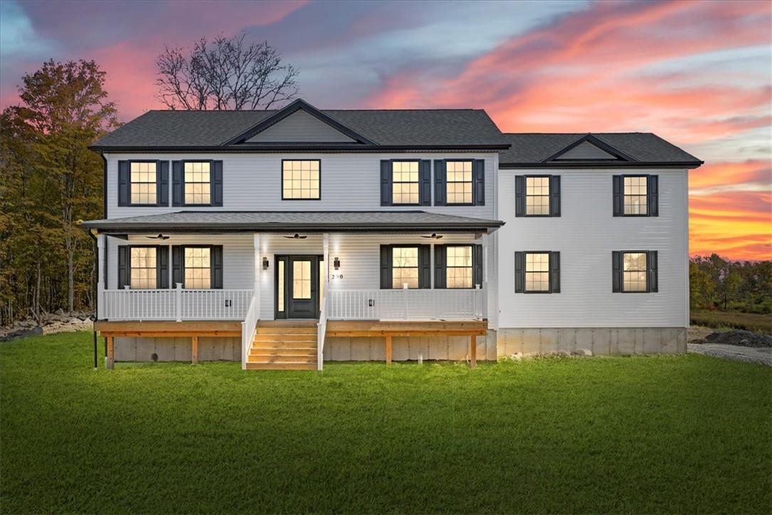 Back house at dusk featuring a porch and a lawn