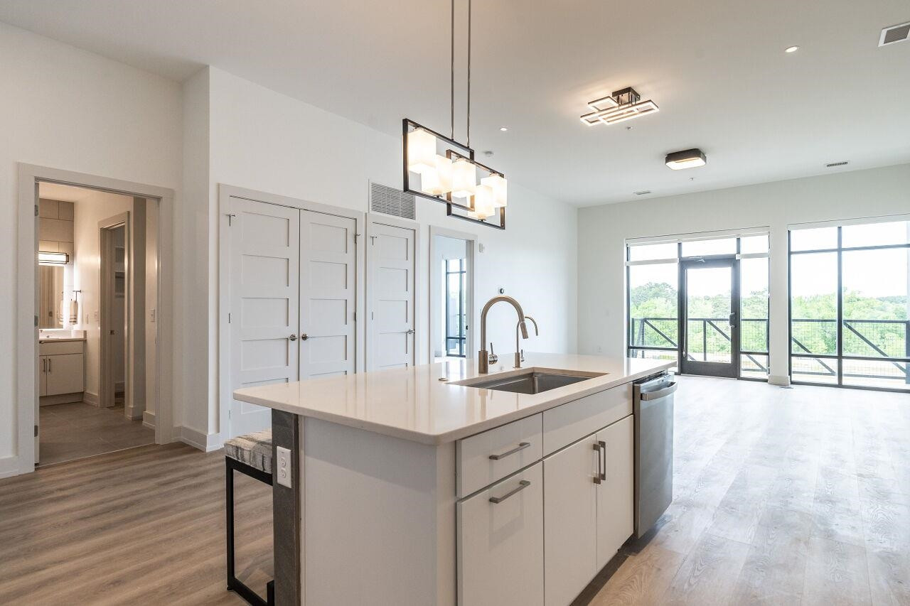 a very nice looking hall with kitchen island a large window a sink and a dining table with chandelier