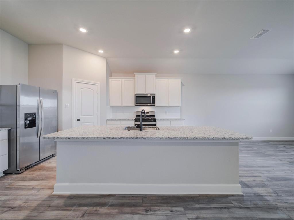 a kitchen with granite countertop a sink a center island stainless steel appliances and cabinets