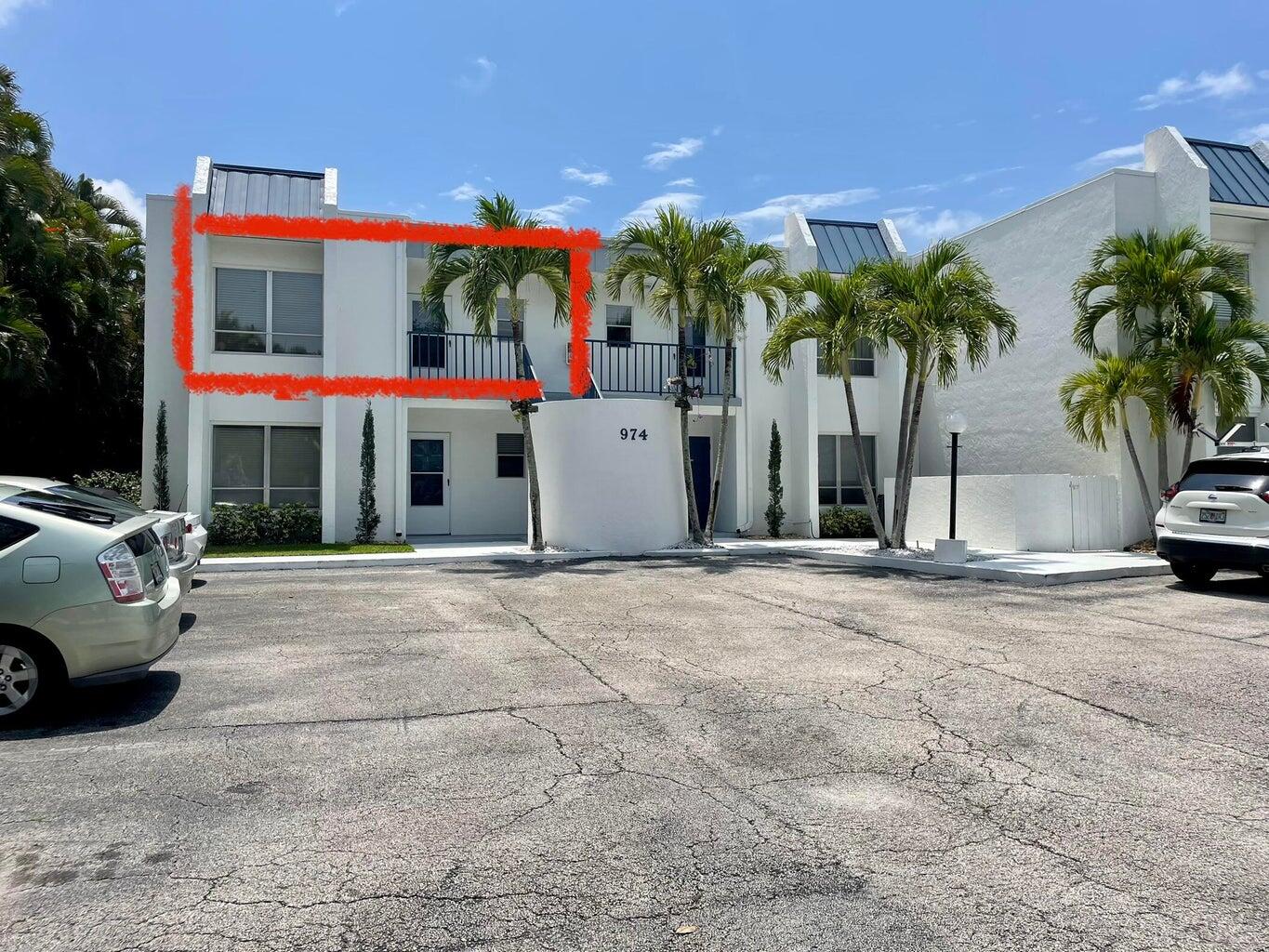 a view of a white building with palm trees and a car parked in front of it