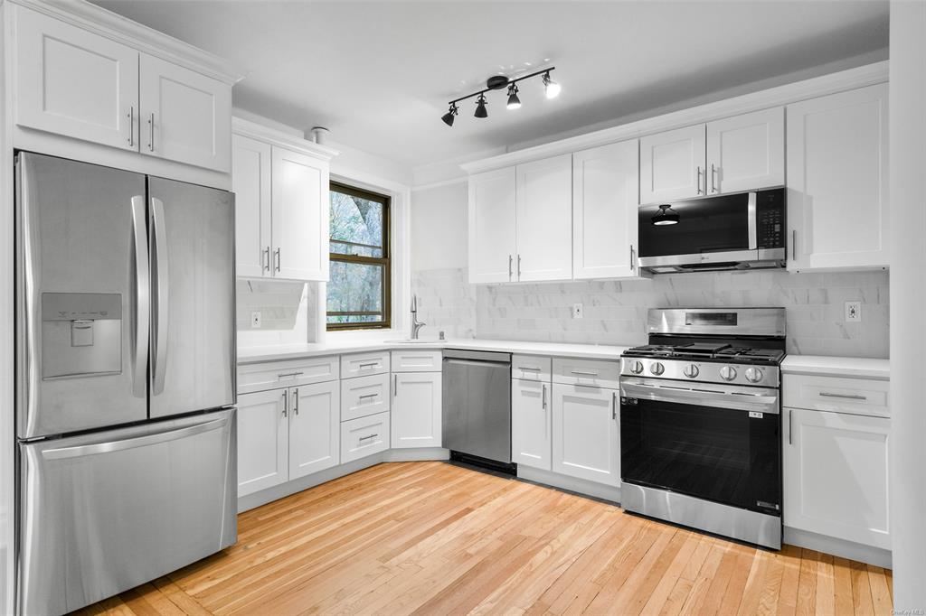 Eat in kitchen featuring stainless steel appliances, light hardwood / wood-style floors, white cabinets, and tasteful backsplash