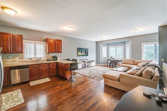 a large living room with stainless steel appliances granite countertop a couch wooden cabinets and a wooden floor