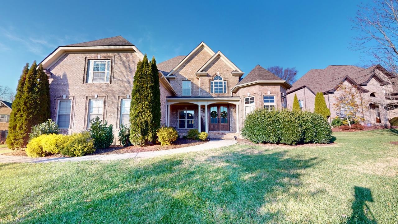 a view of a brick house with a big yard and large trees