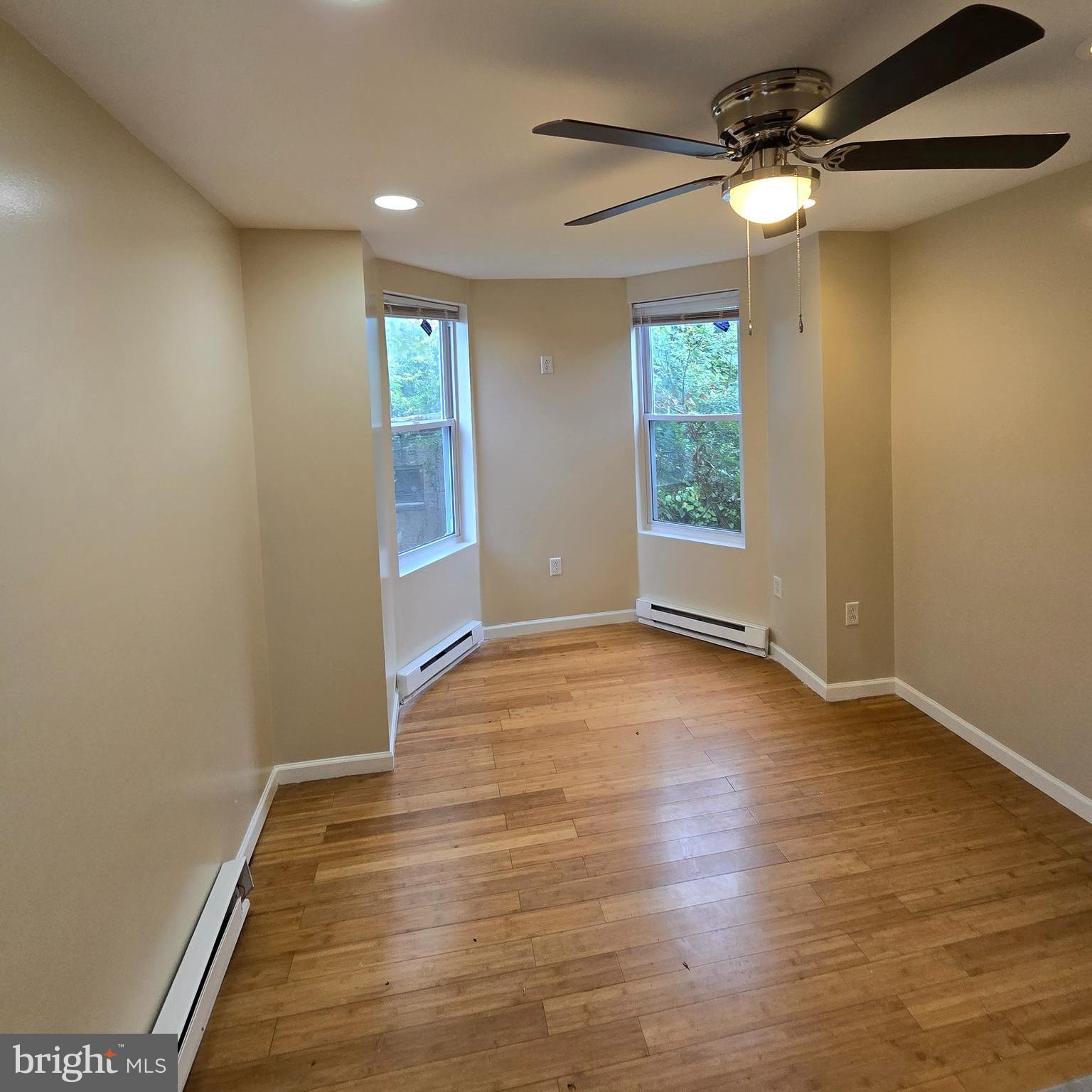 an empty room with wooden floor fan and windows