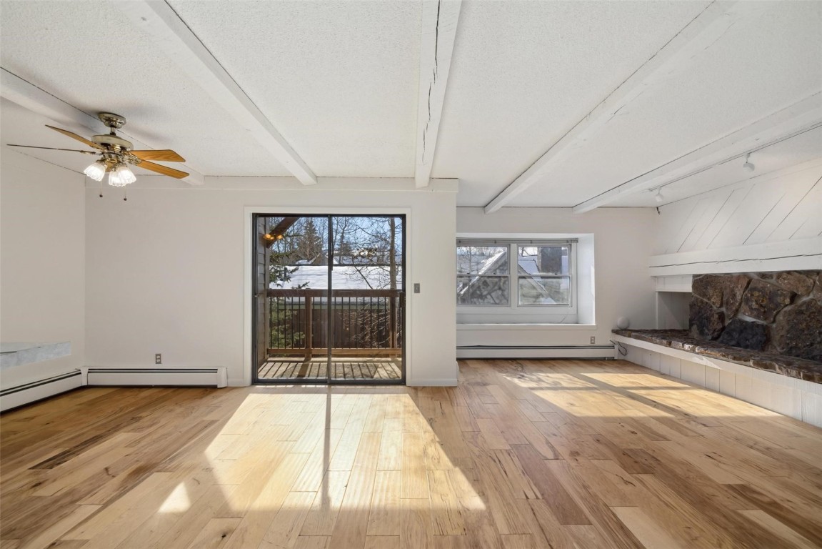 Unfurnished living room with a baseboard heating unit, ceiling fan, light wood-type flooring, a textured ceiling, and beamed ceiling