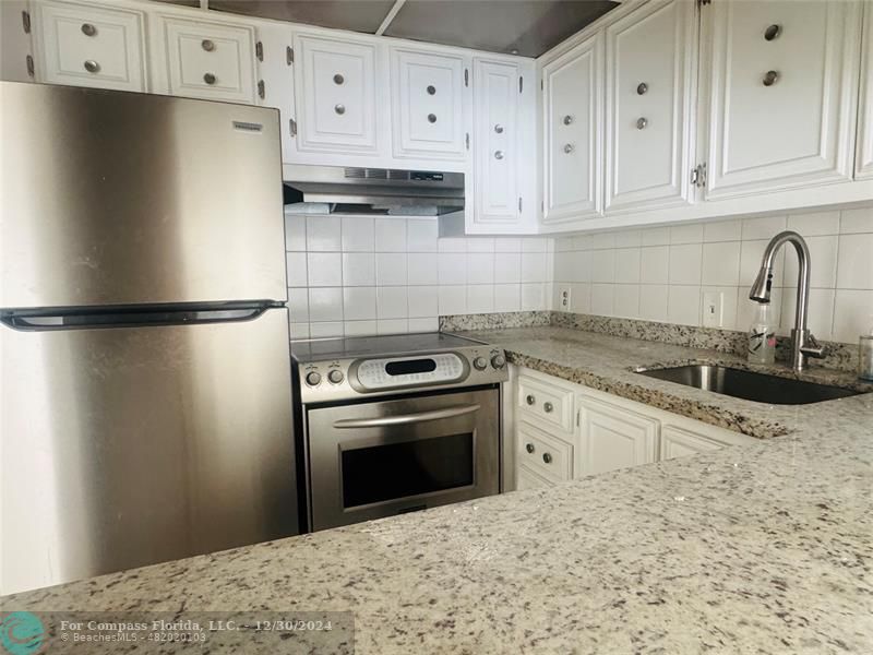 a kitchen with granite countertop a refrigerator sink stove and cabinets