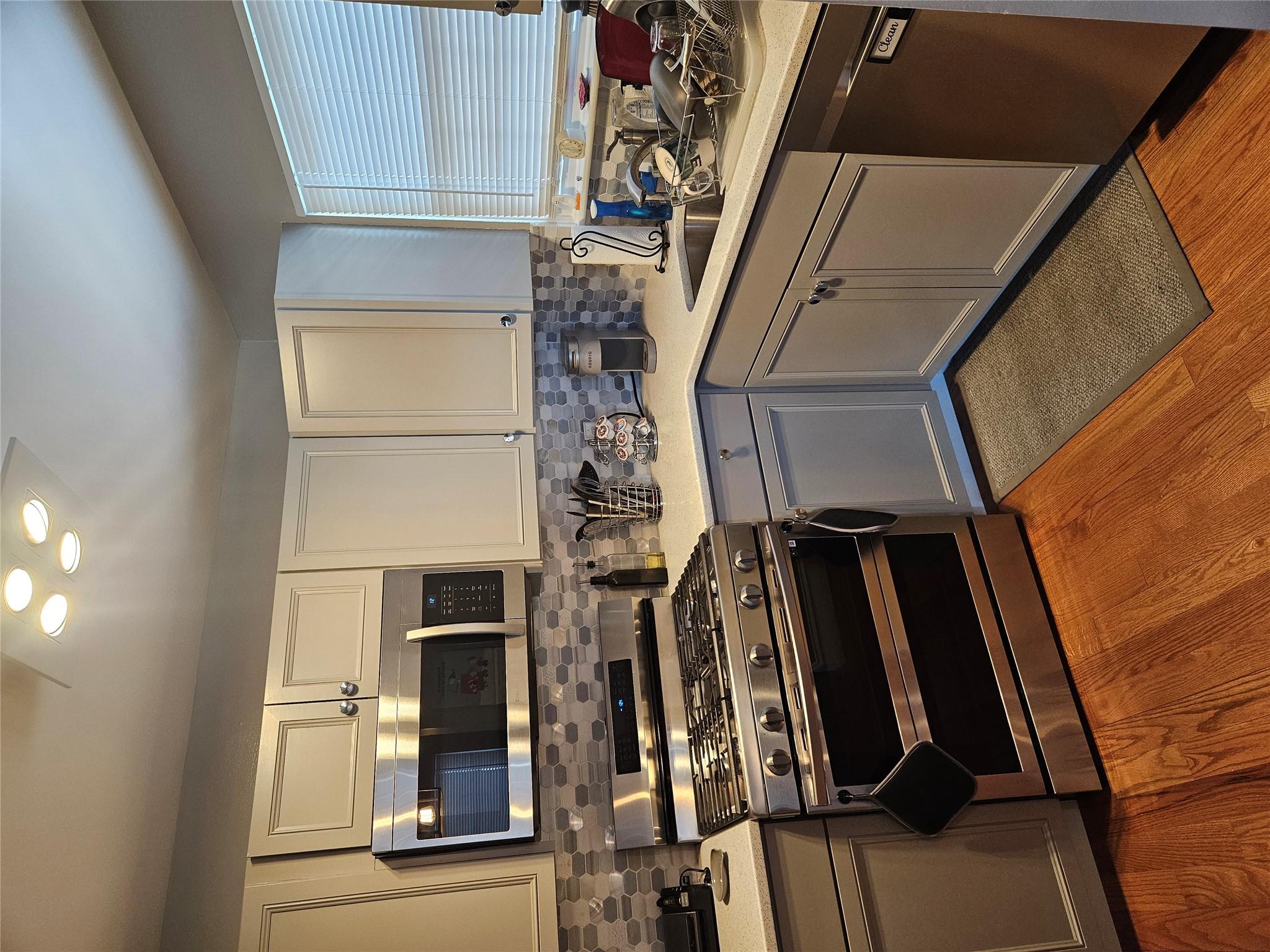 Kitchen featuring stove, tasteful backsplash, dishwashing machine, hardwood / wood-style flooring, and gray cabinets