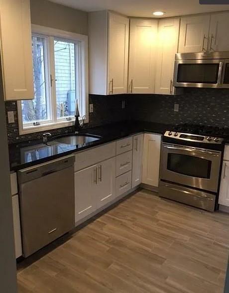 Kitchen with light hardwood / wood-style flooring, stainless steel appliances, sink, and white cabinets