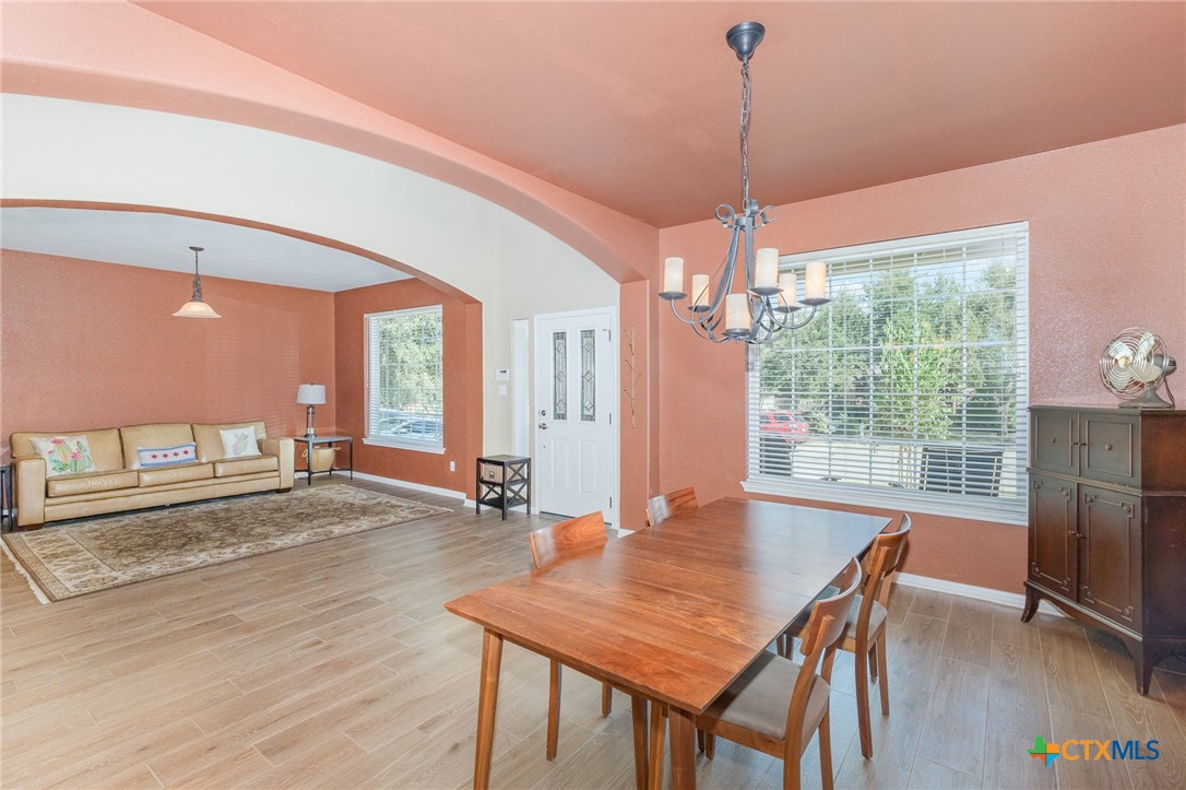 a dining room with wooden floor a chandelier a glass table and chairs