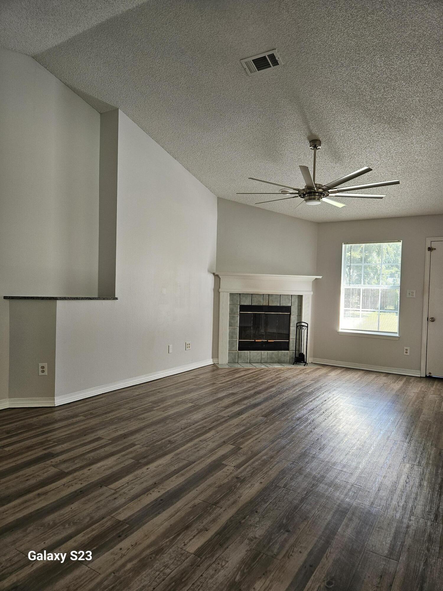 an empty room with wooden floor fireplace and windows